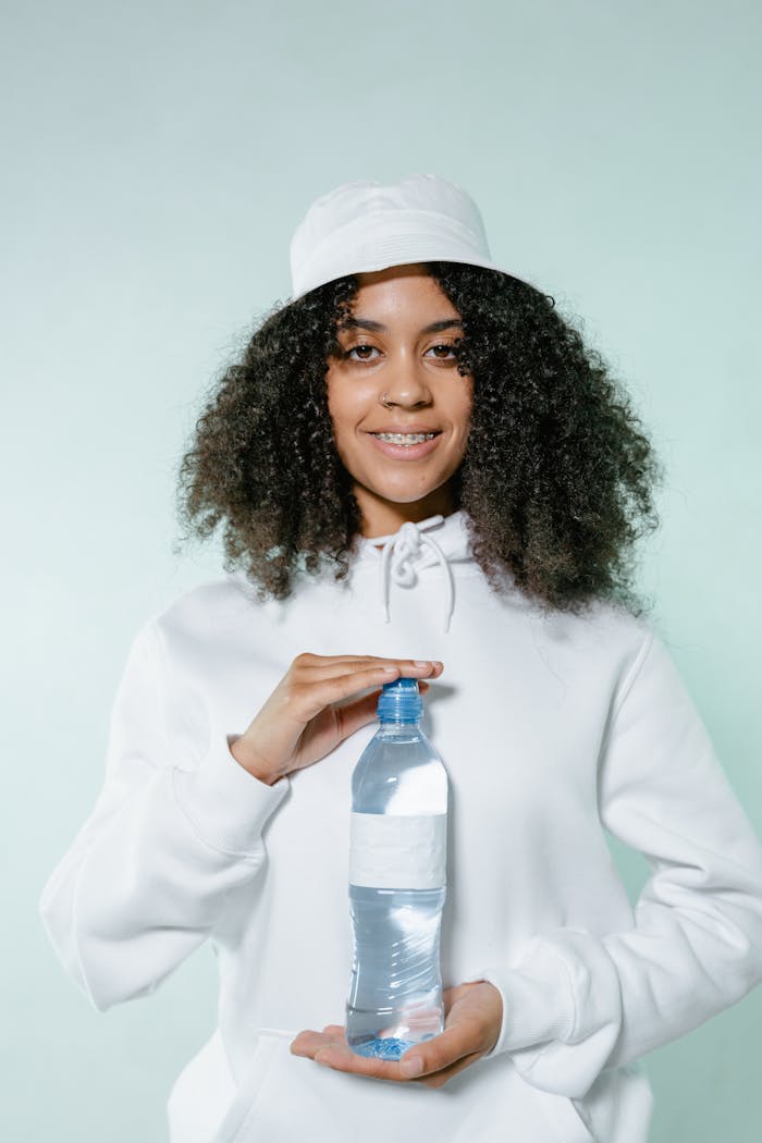 A woman with curly hair in a white outfit smiling while holding a water bottle.
