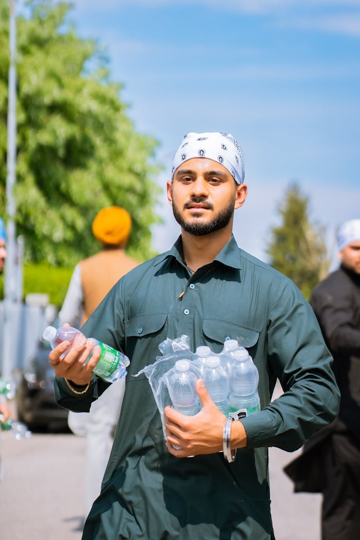 A young man handing out bottled water on a sunny day, engaging in community service.